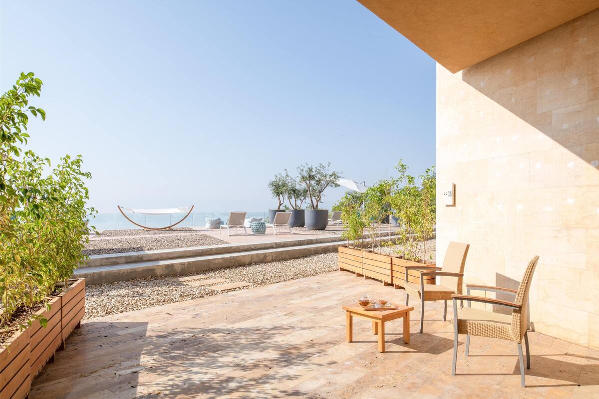 A terrace with outdoor seating, a view of the beach, and a clear sky.