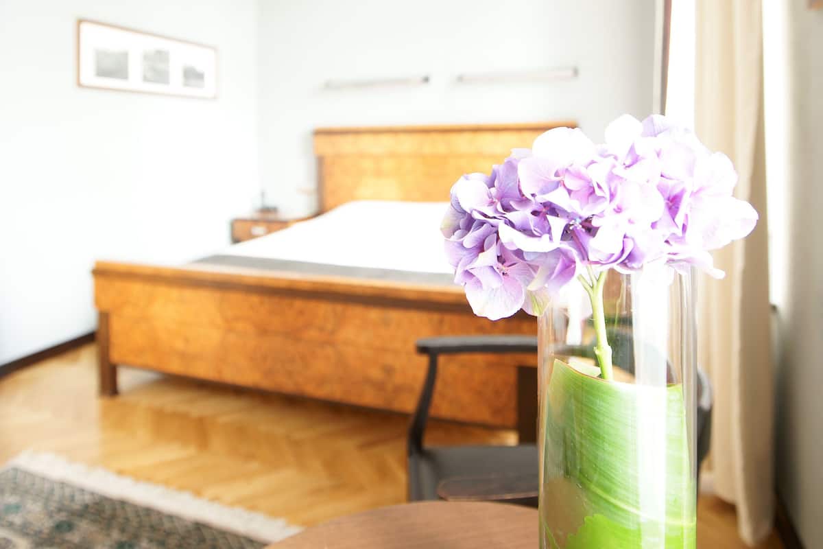 A room with a bed, a wooden headboard, a vase with purple flowers, and a green drink in a glass.