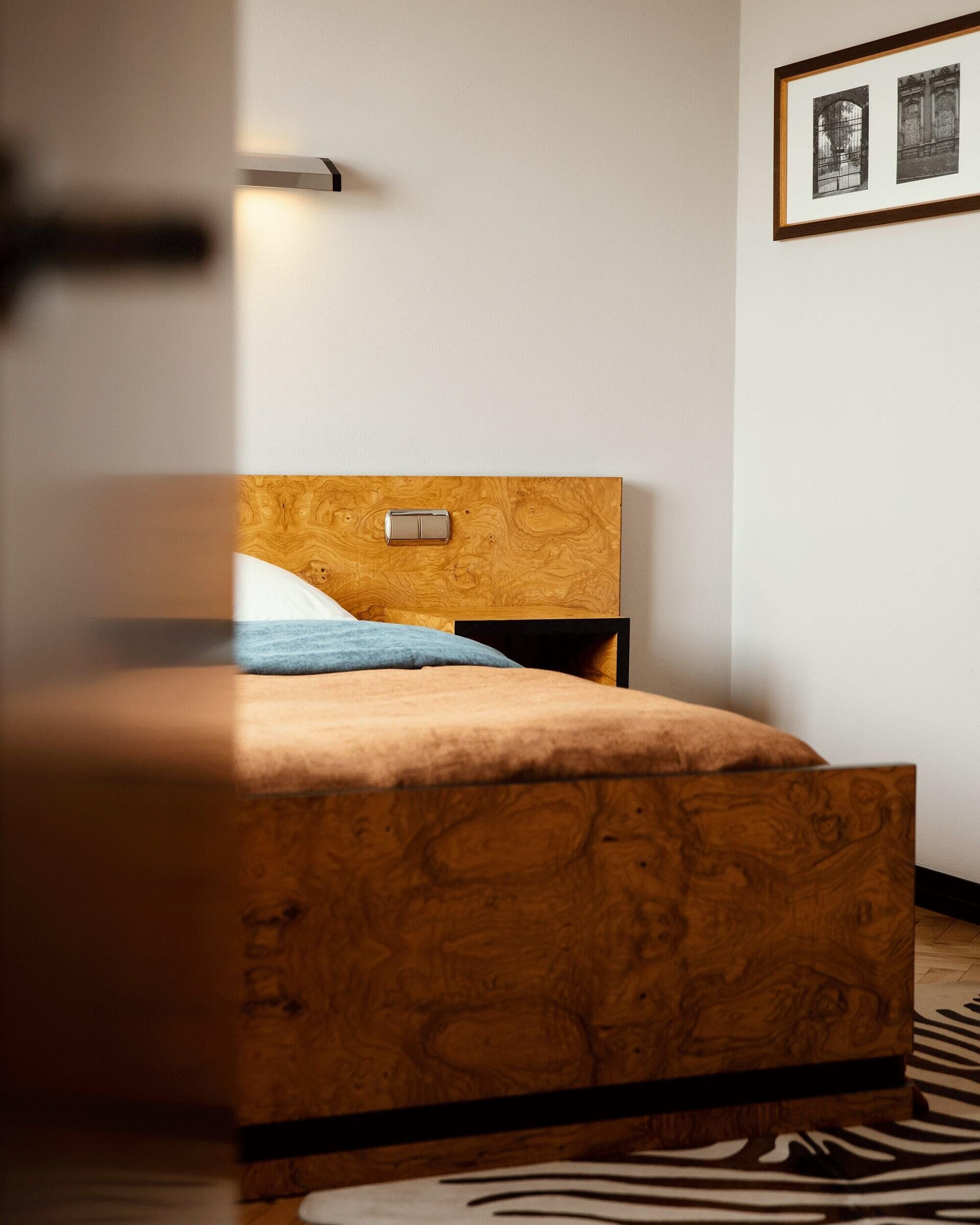 A modern bedroom with a wooden headboard, a bed with a blue pillow, a nightstand, and a zebra-patterned rug.
