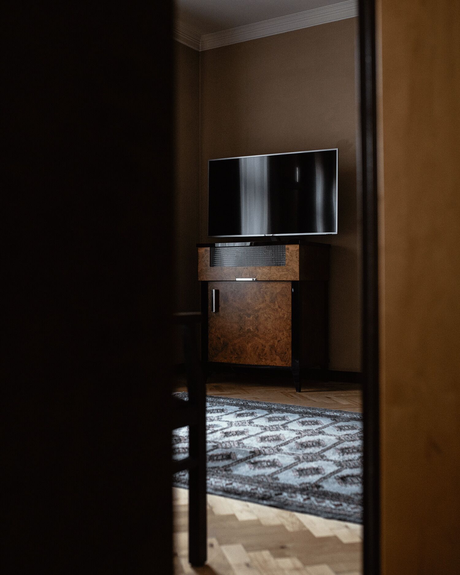 Ein Zimmer mit einem an einer Holzkabine montierten Flachbildfernseher, einem gemusterten Teppich auf dem Boden und einer teilweise geöffneten Tür.