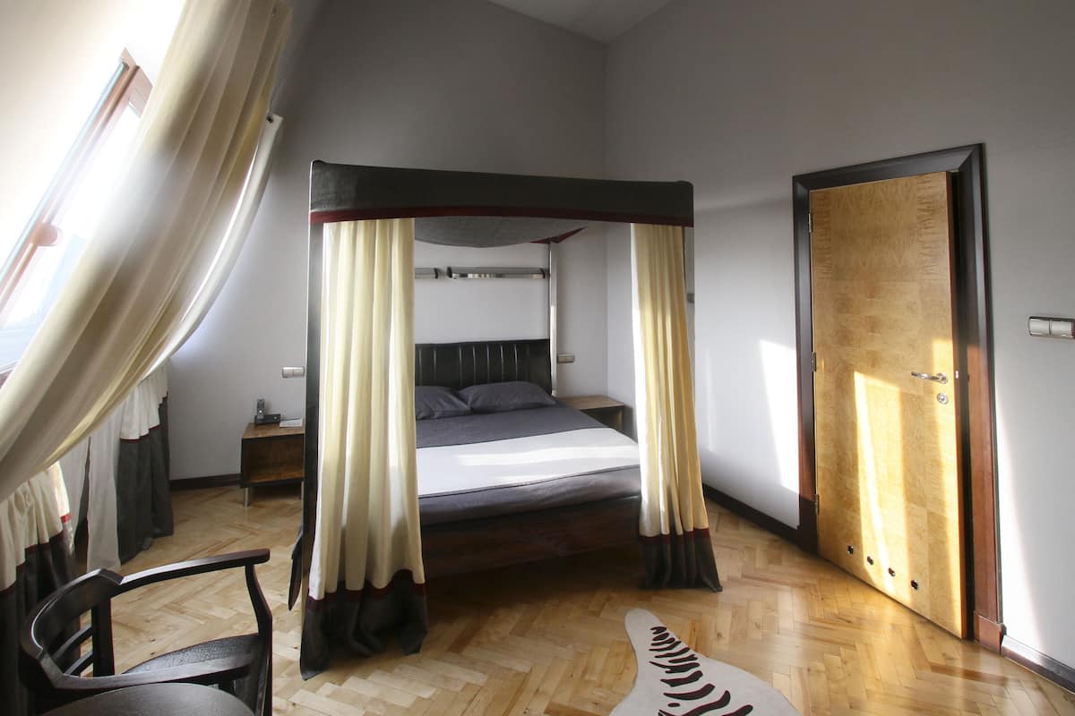 A bedroom with a four-poster bed, a wooden door, and a window with curtains.