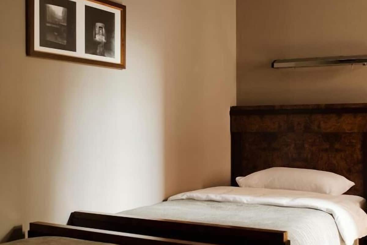 A bedroom with a single bed, a second bed in the foreground, a stone wall, and two framed pictures on the wall.