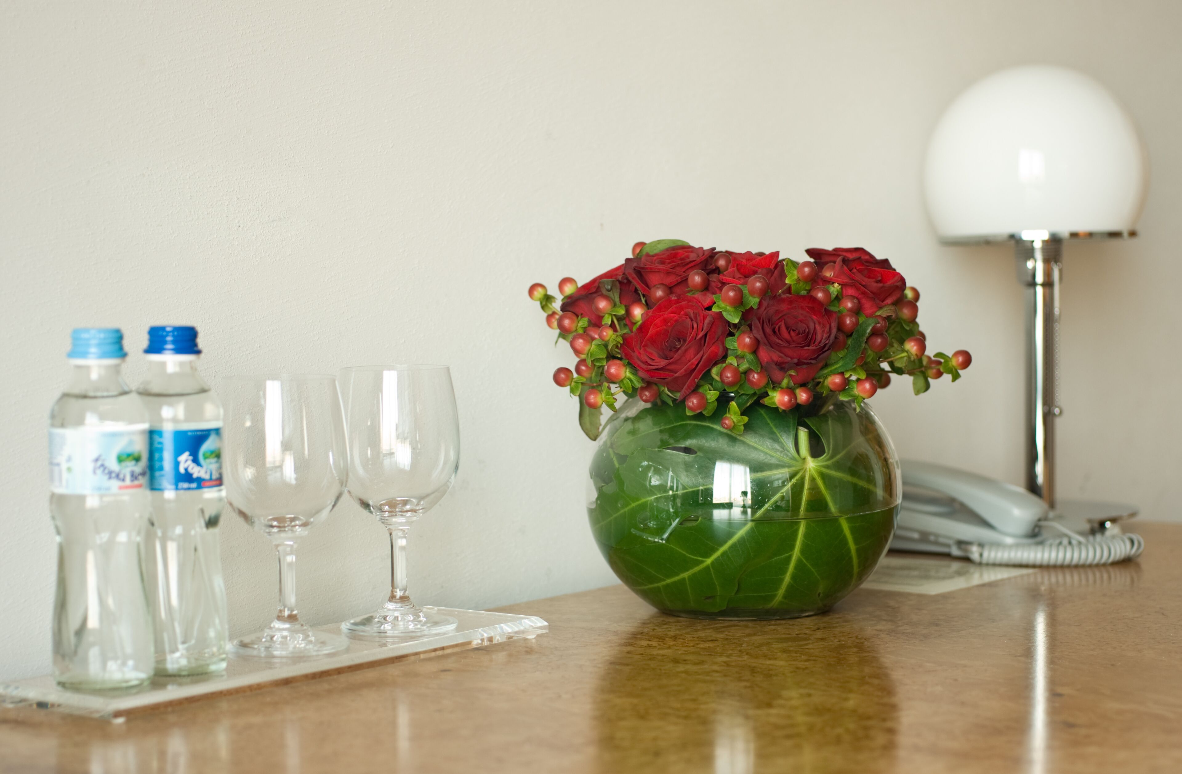 A table with a vase of red roses, two water bottles, and two wine glasses.