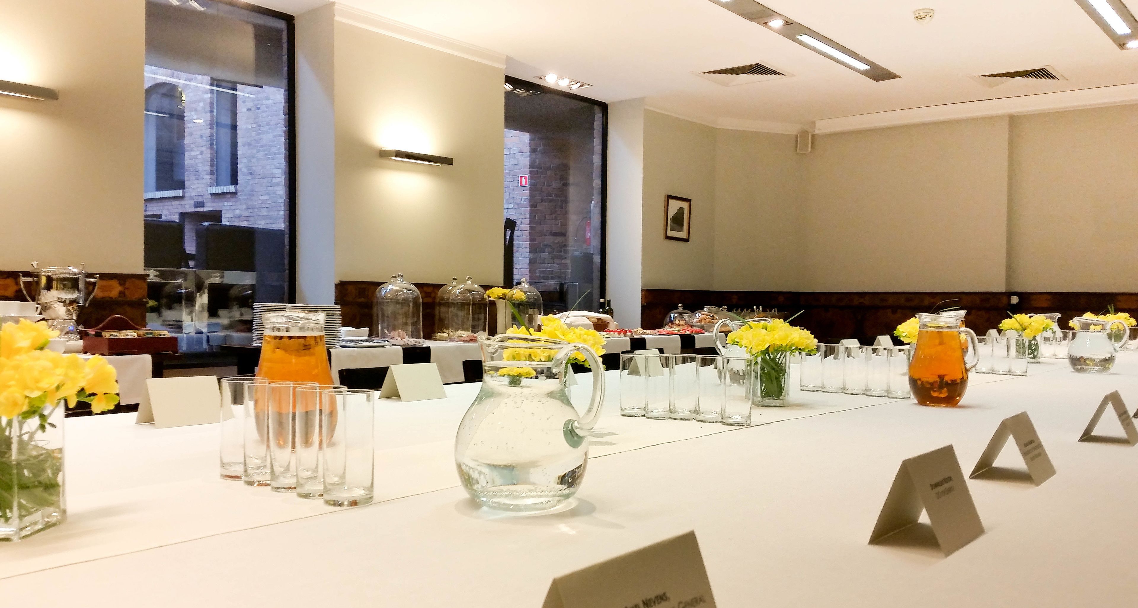 A conference room with a long table set for a meeting, equipped with nameplates, glassware, and floral centerpieces.