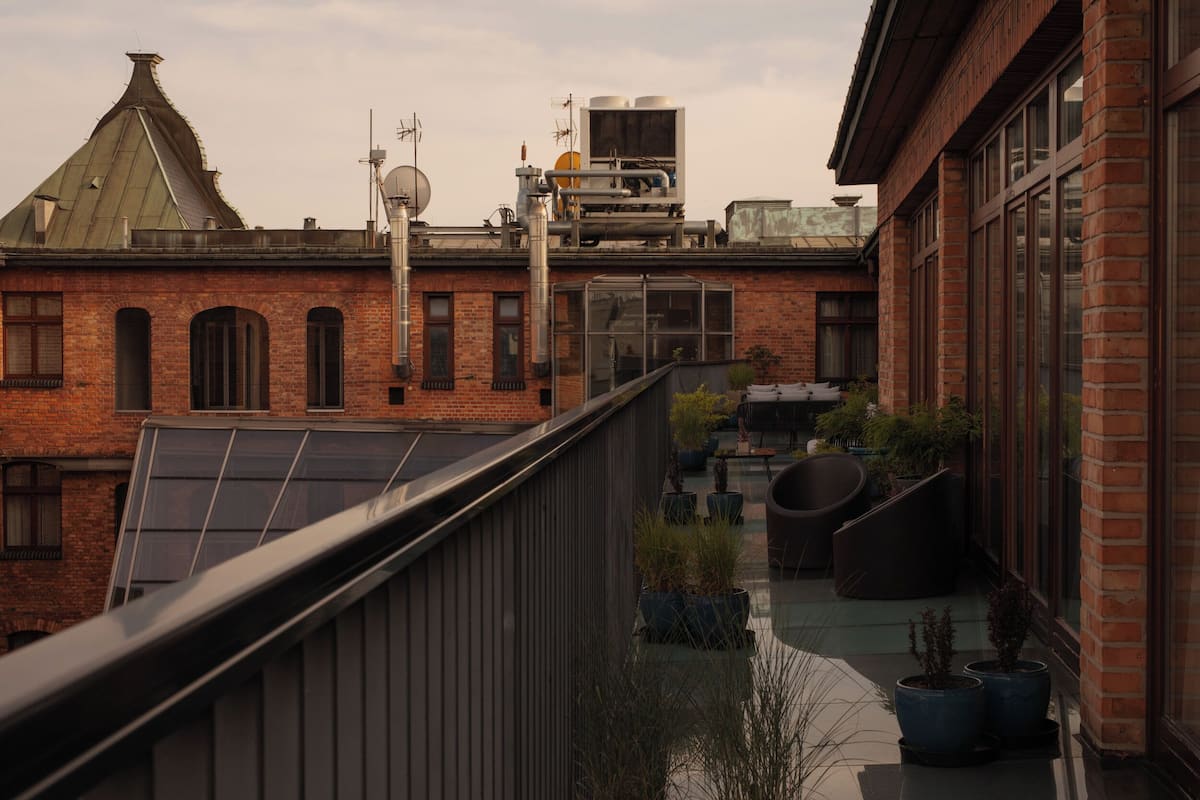 A rooftop terrace with a brick building, solar panels, and potted plants.