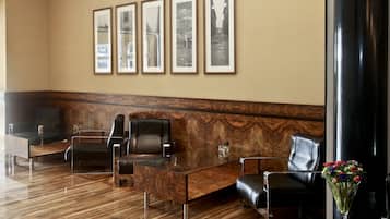 Un vestíbulo con mostrador de recepción, dos sillones de cuero negro, una mesa de centro de vidrio y cuadros enmarcados en la pared.