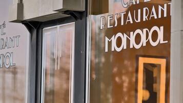 Un café con grandes ventanales y un letrero que dice "CAFÉ RESTAURANT MONOPOL".