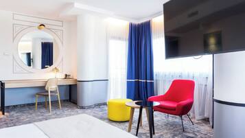 A hotel room with a bed, a desk, a chair, a TV, and a window with curtains.