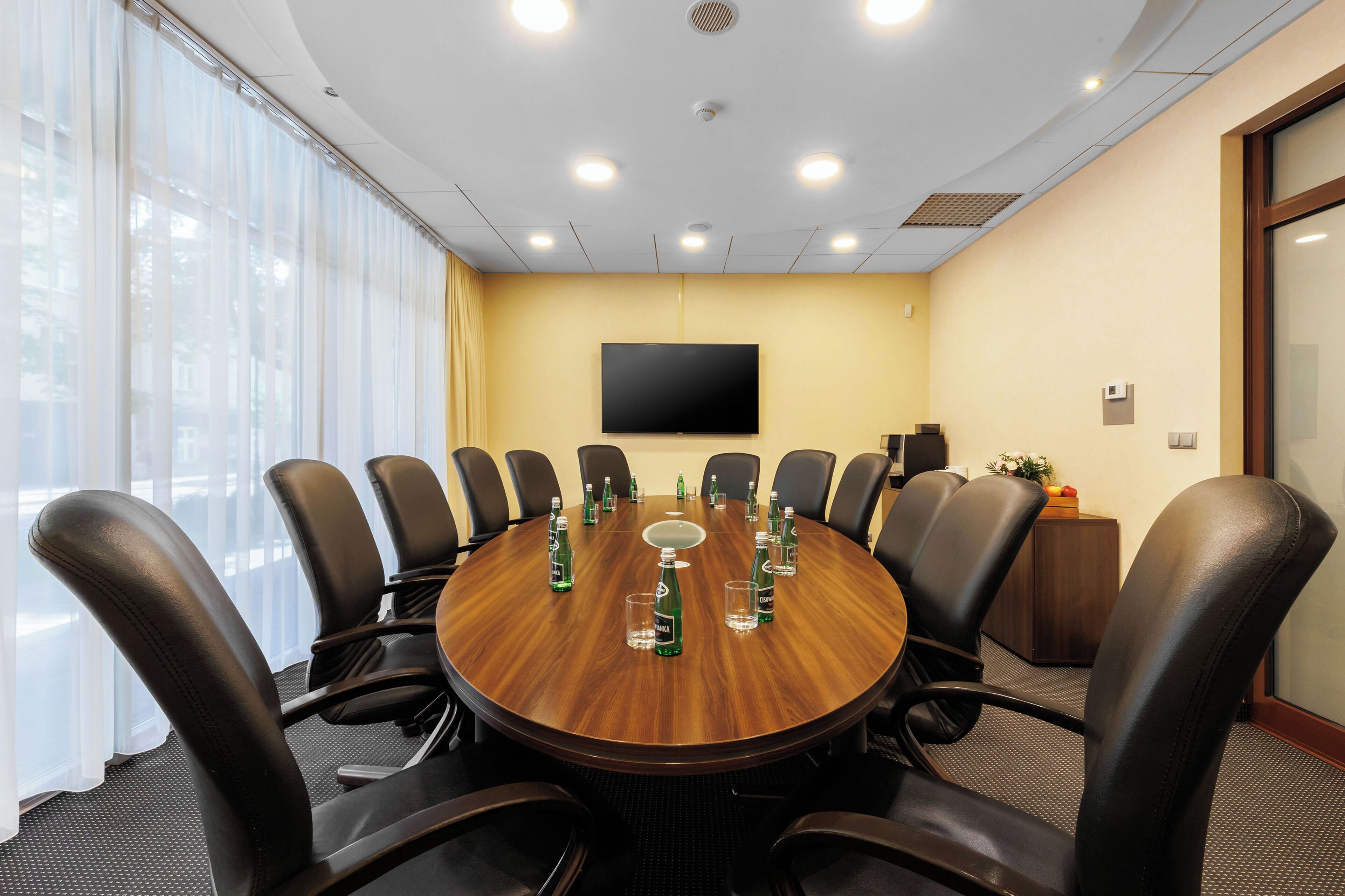 Une salle de conférence équipée d’une table ronde, de fauteuils en cuir noir et d’un téléviseur à écran plat fixé au mur.