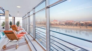 Une chambre d’hôtel moderne dotée de grandes fenêtres donnant sur une rivière et sur le paysage urbain.