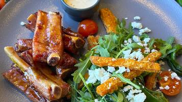 Une assiette de nourriture comprenant des travers de porc, des légumes verts et un petit bol de sauce.