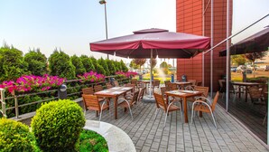 Une terrasse extérieure avec des tables et des chaises, entourée de verdure et de fleurs.