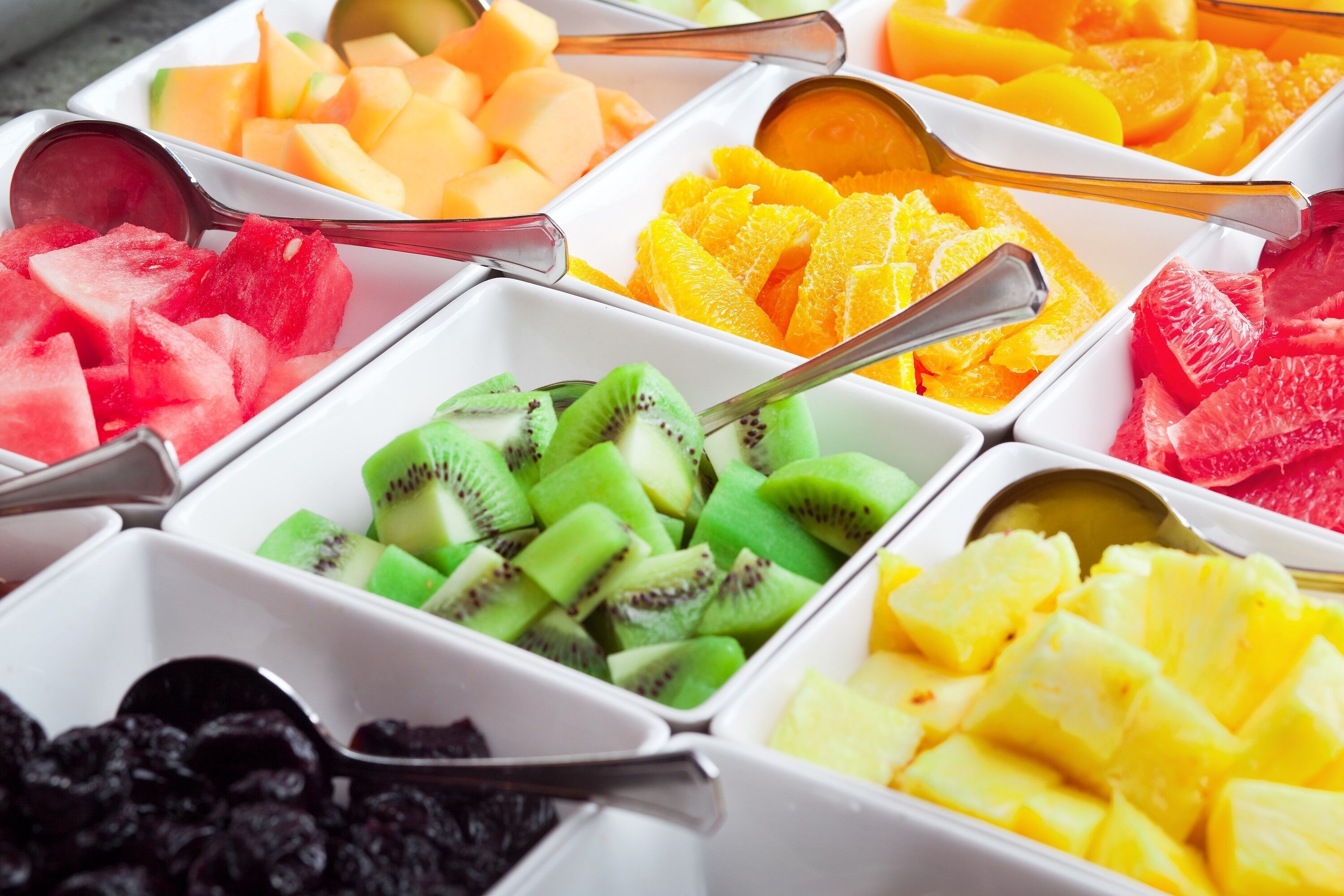 A variety of fruits in white bowls with spoons.