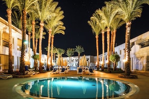 A pool area with palm trees, lounge chairs, and umbrellas. - Xperience St. George Homestay (Sharm El Sheikh)