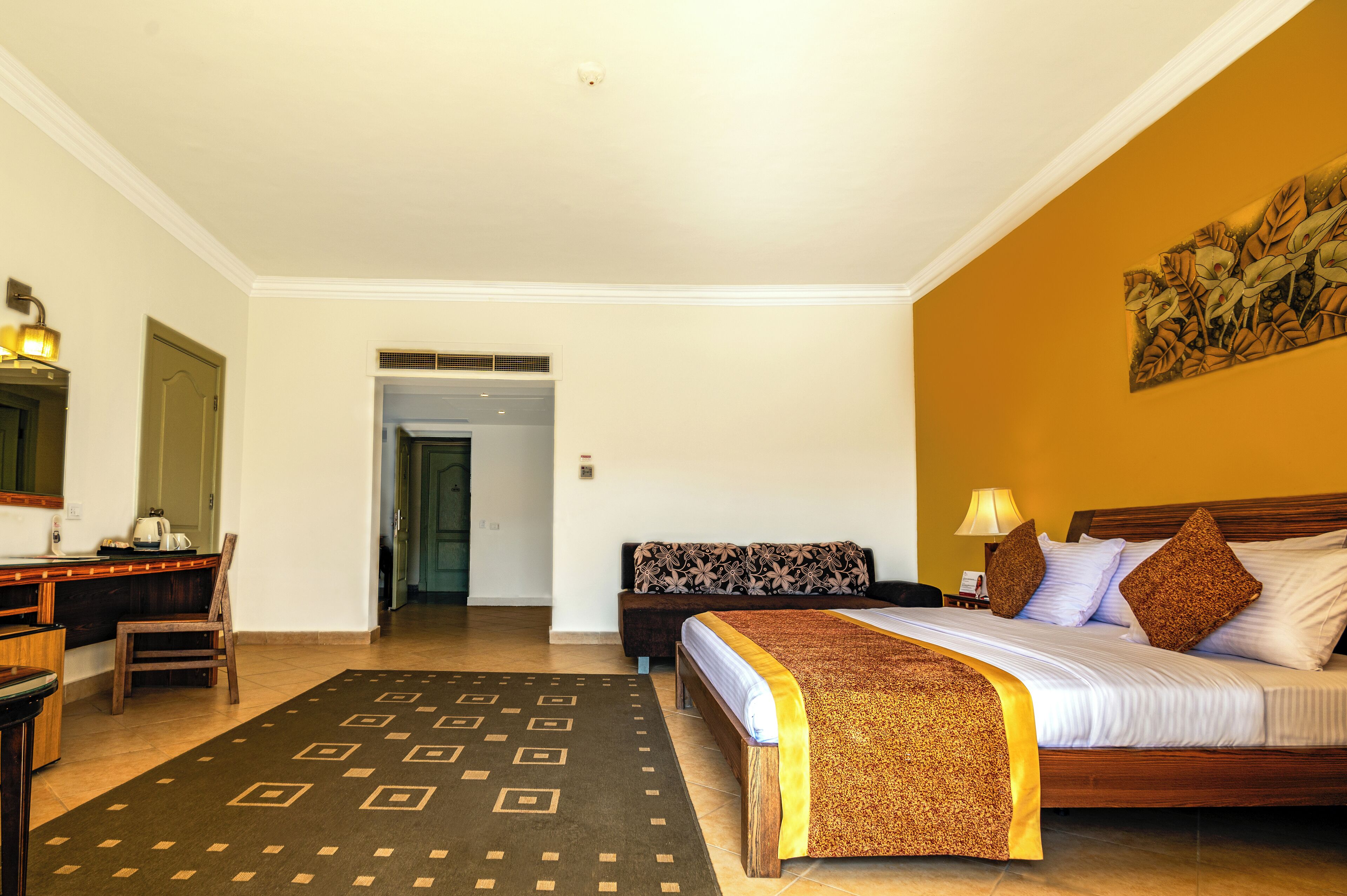 A hotel room with a bed, a desk, a chair, a lamp, and a painting on the wall.