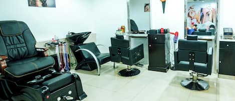 A salon with multiple black salon chairs, a large mirror, and a clock on the wall.