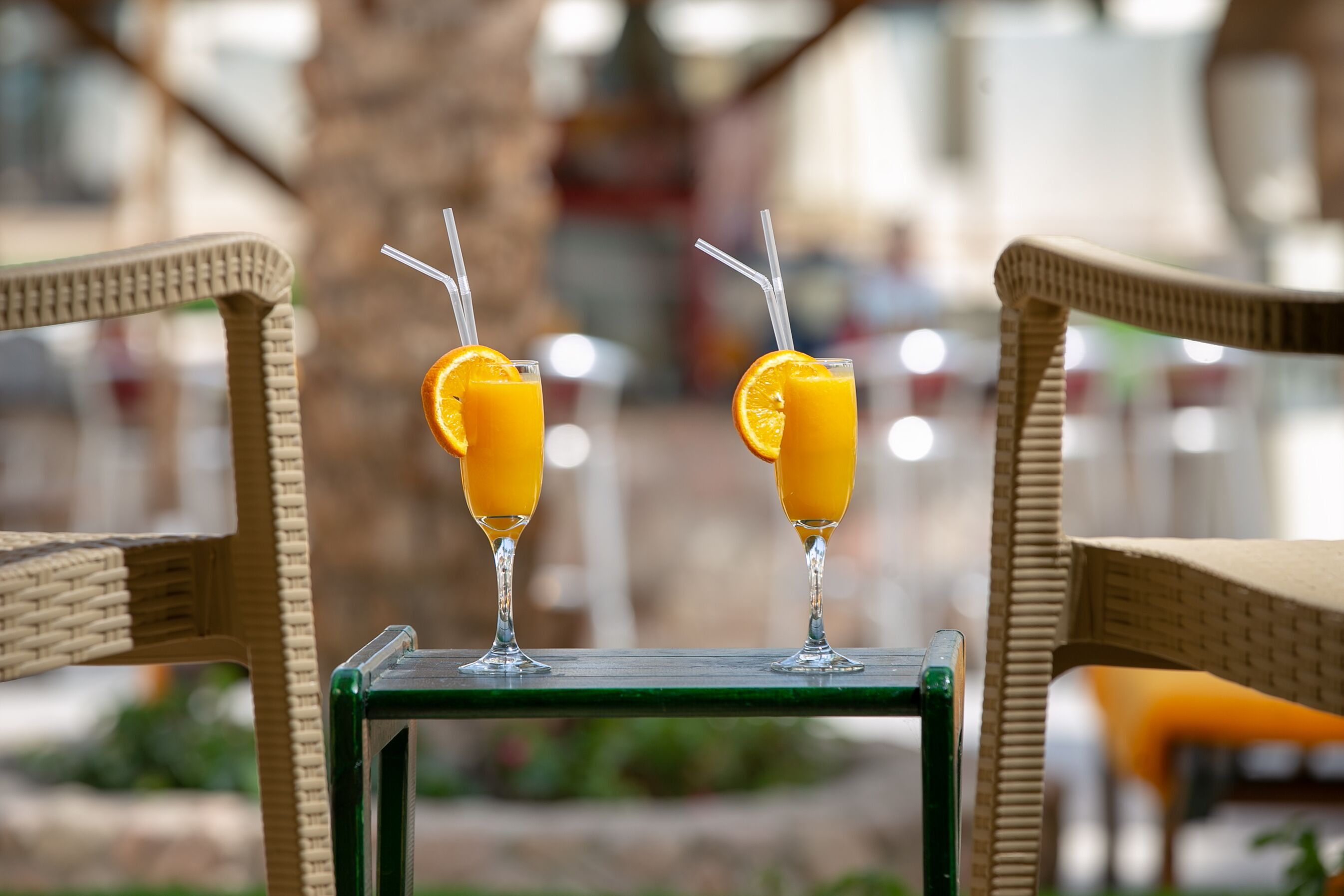 Dos bebidas con rodajas de naranja sobre una mesa, entre sillas de mimbre.