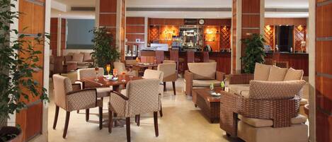 Vestíbulo de hotel con zona de bar, disposición de asientos y mostrador de recepción.
