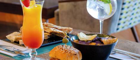 A meal with a burger, a bowl of chips, a glass of orange juice, and a glass of water with lemon and mint.