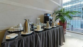 Uma mesa de buffet com diversos recipientes de servir e uma máquina de café.