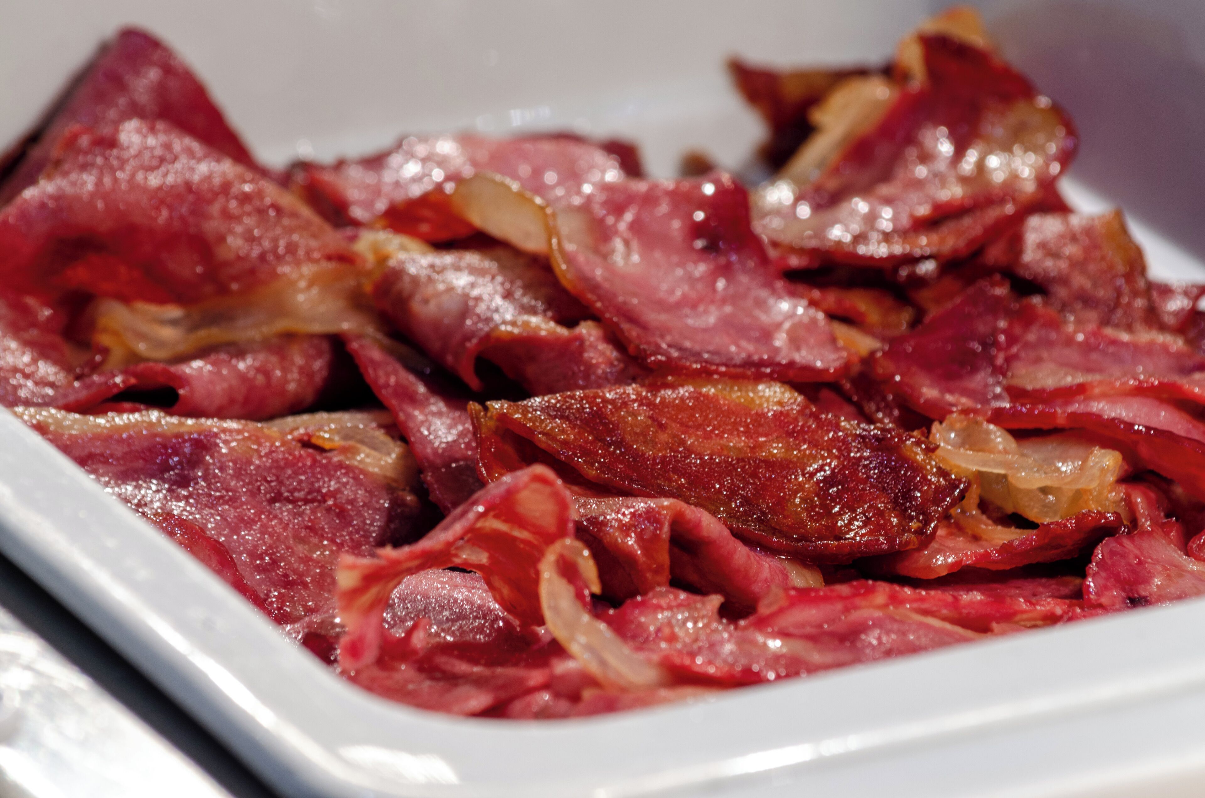 A white rectangular plate with raw bacon strips and onions.