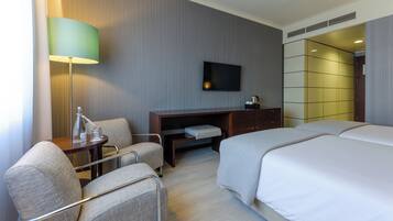 A hotel room with a bed, a desk, two chairs, a TV, and a lamp.