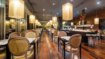 A restaurant with a long counter, multiple tables, and hanging pendant lights.