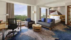 Habitación de hotel con escritorio, dos sillas, sofá, cama y vistas a la ciudad.