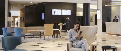 A modern lobby with seating areas, a reception desk, and a digital display.