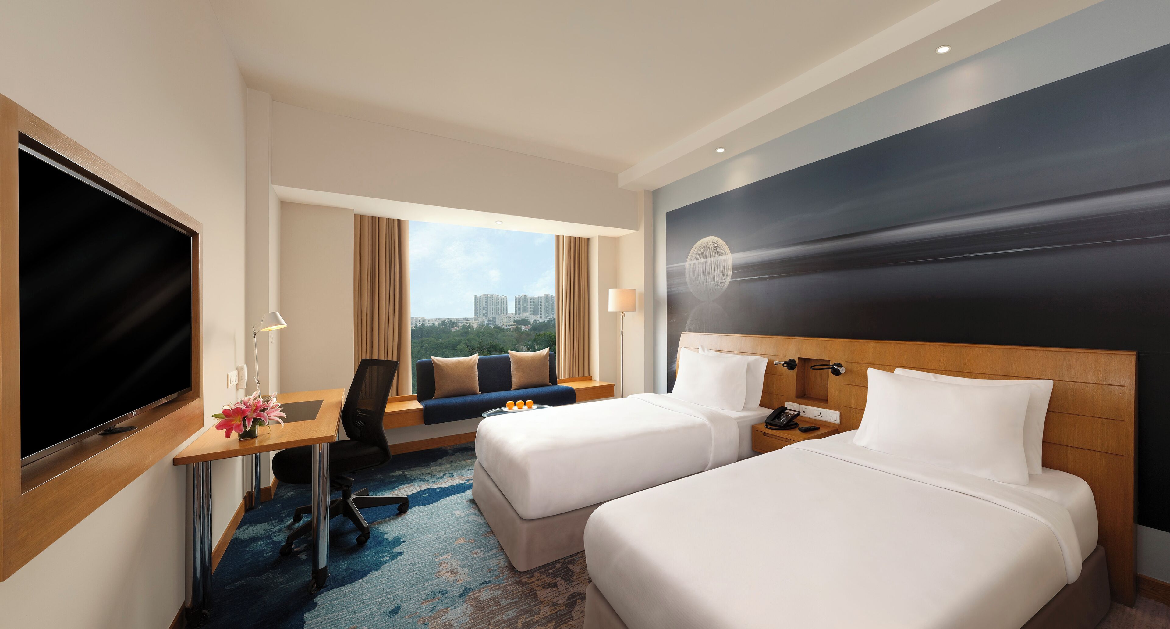 Habitación de hotel con cama, escritorio con televisor, una silla y vista a la ciudad.
