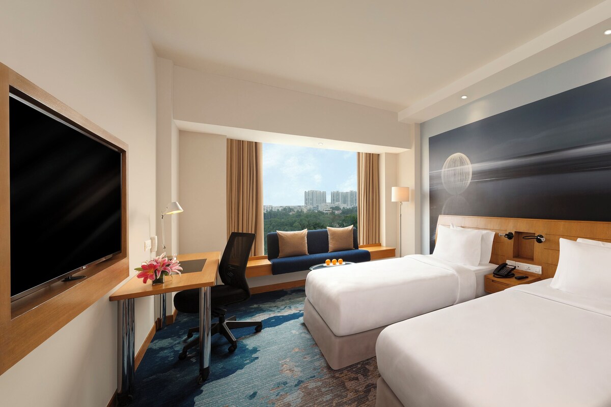 Een hotelkamer met een bed, een bureau met een televisie, een stoel en uitzicht op de stad.