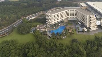 An aerial view of a hotel with a swimming pool, surrounded by greenery and a parking area.