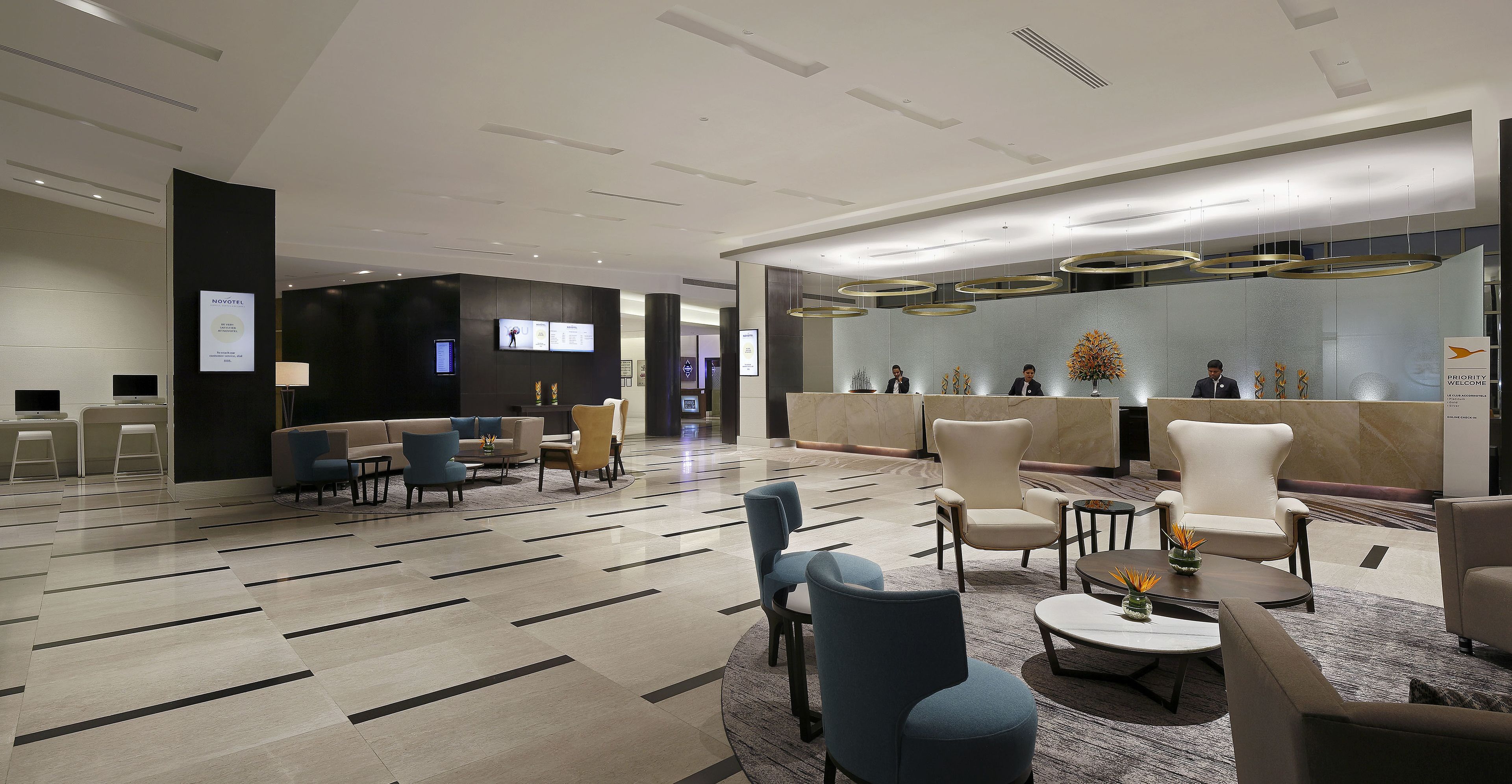 A modern hotel lobby with a reception desk, seating area, and a decorative wall with a clock.