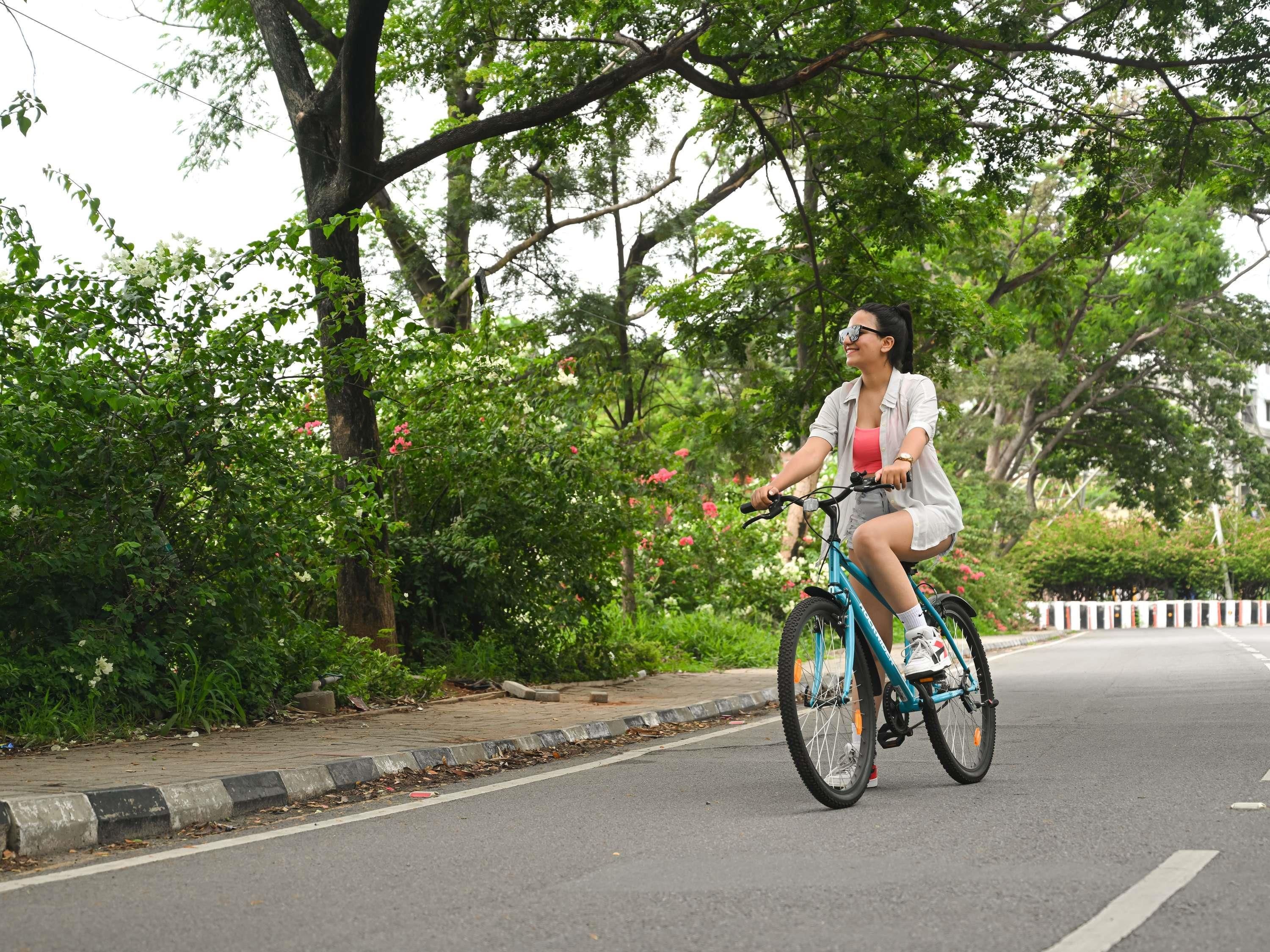 A person riding a bicycle on a road with trees and flowers on the side.