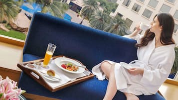 A person seated on a blue sofa with a tray of breakfast items, including a glass of orange juice, a plate of fruit, and a croissant.