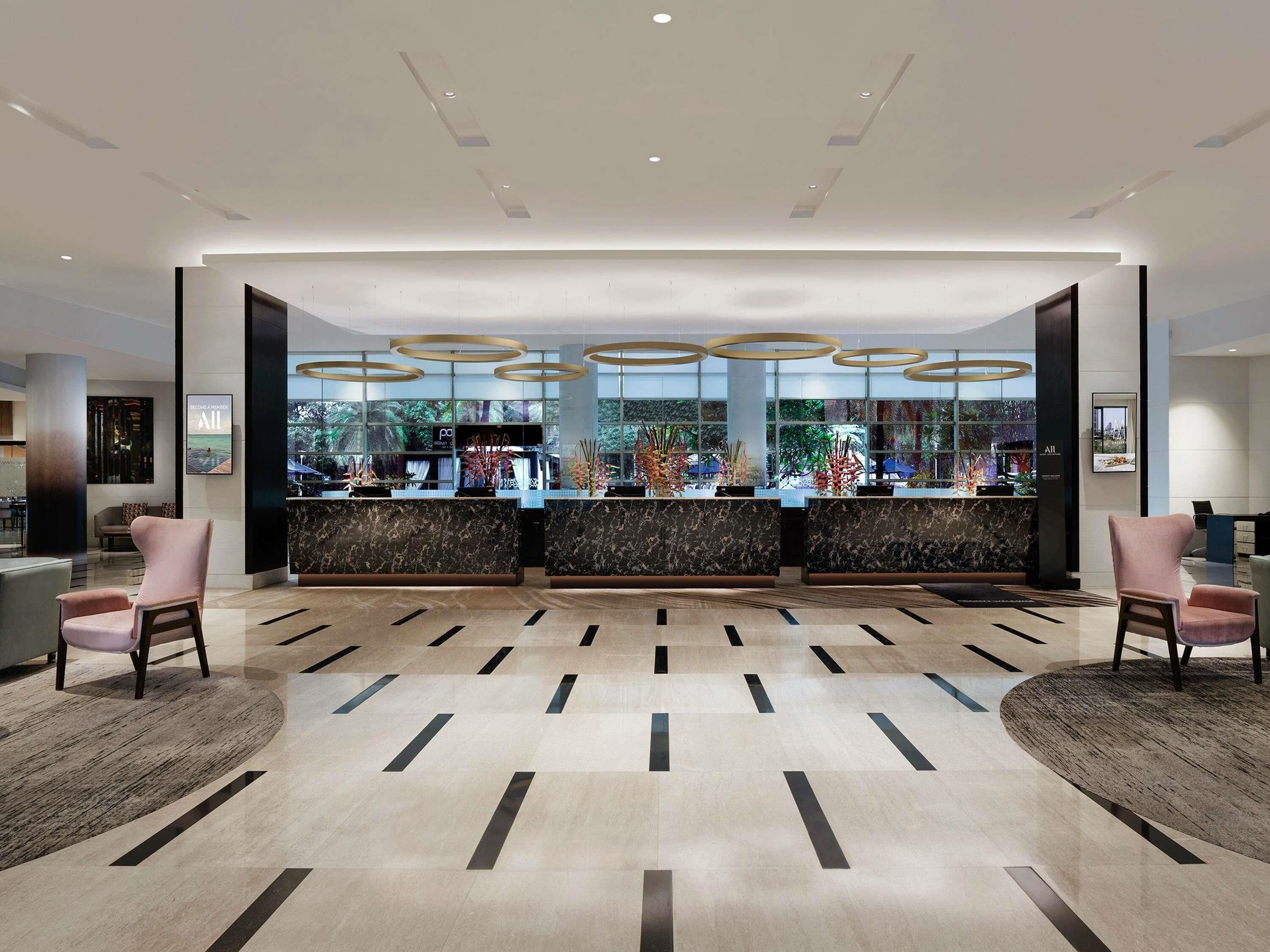 A modern reception area with a marble counter, two pink chairs, and a view of the outdoors through large windows.