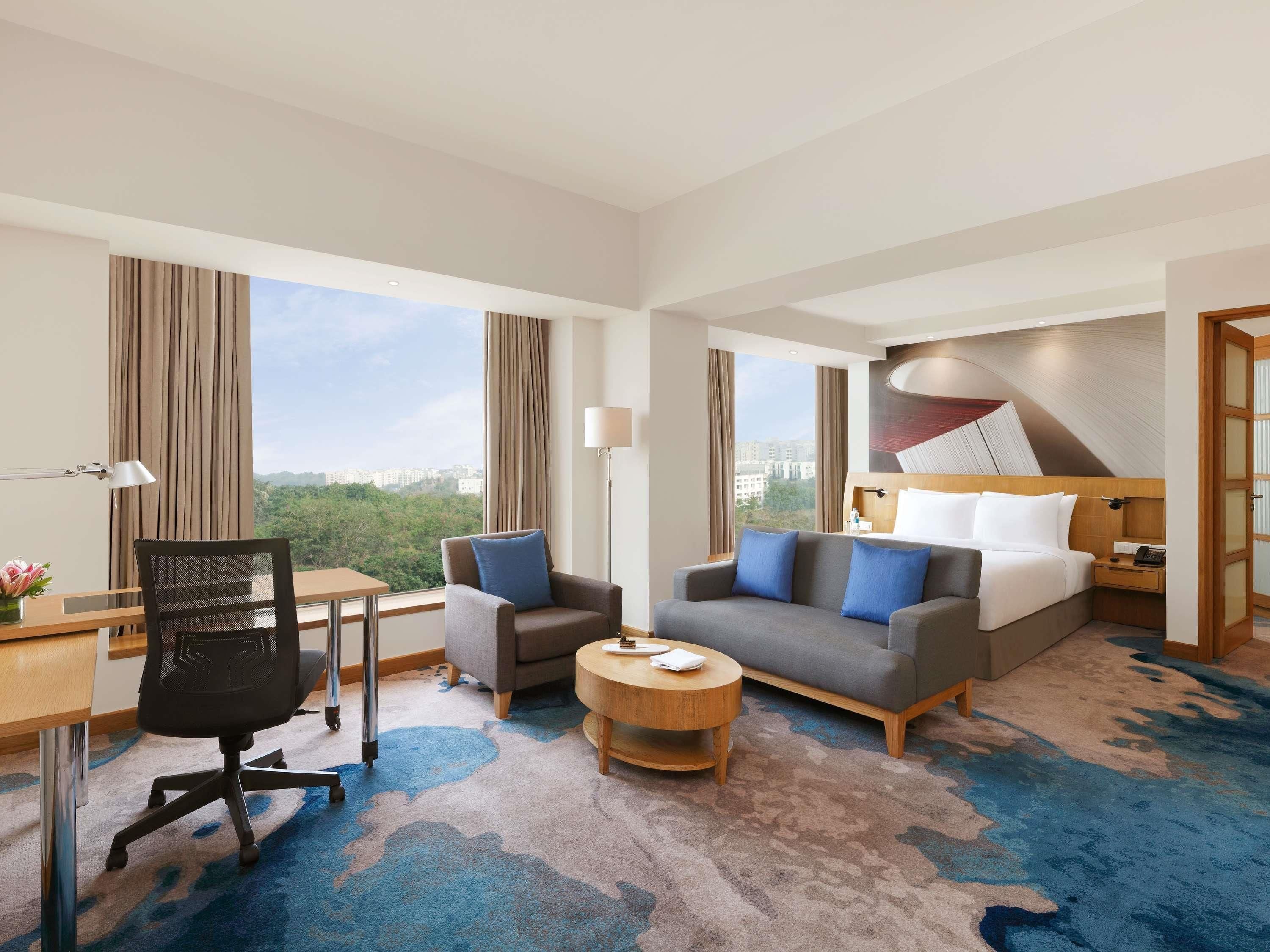 A hotel room with a desk, office chair, sofa, and a bed with a headboard.