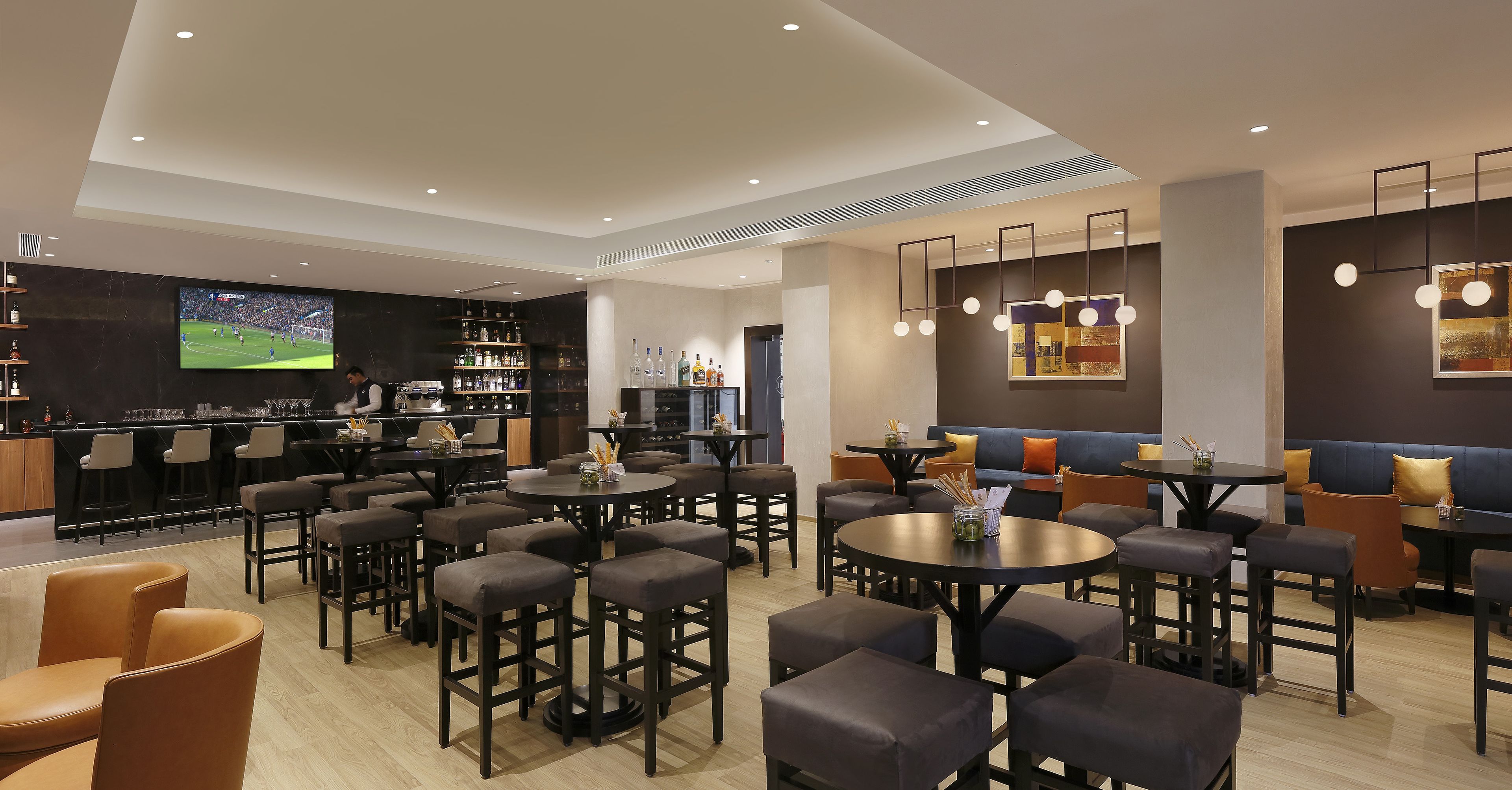 Un espace bar moderne offrant de nombreuses options de sièges, un téléviseur diffusant un événement sportif et divers équipements et services de bar.