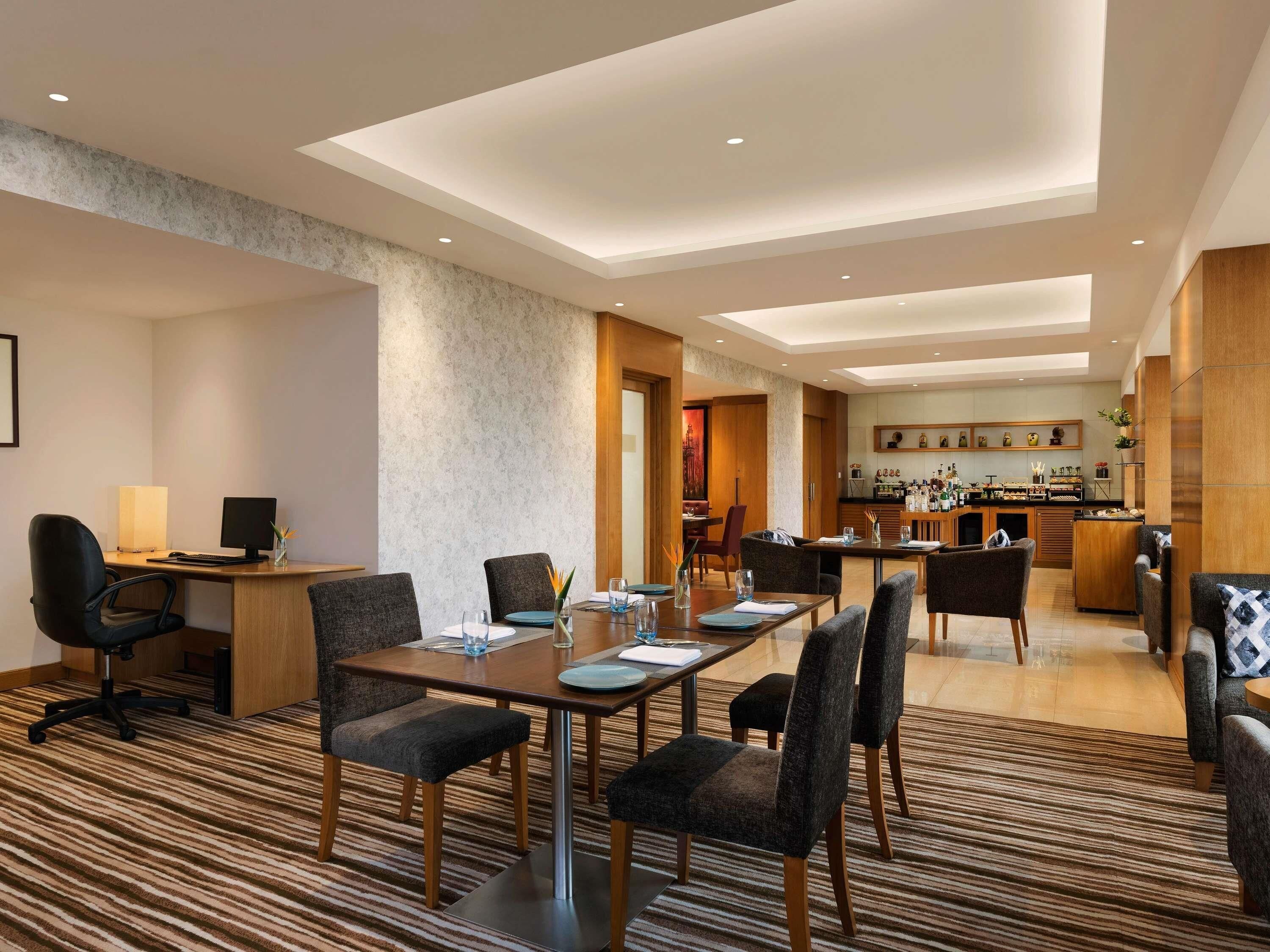 A hotel room with a dining area, a kitchen, and a seating area with a patterned carpet.