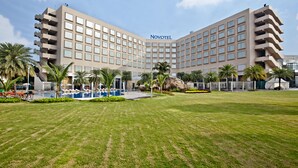Un hotel Novotel con un amplio césped, palmeras y una piscina.