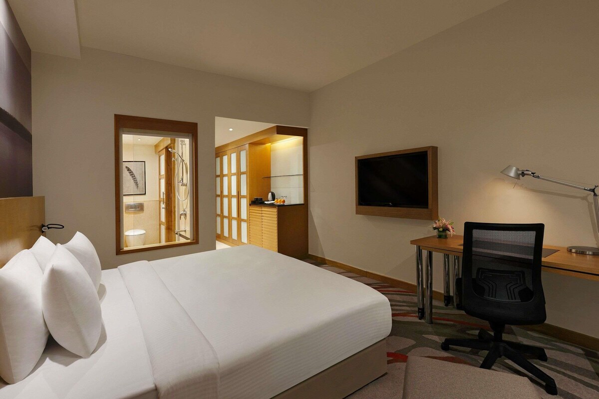 A hotel room with a bed, desk, chair, TV, and a view into the bathroom.