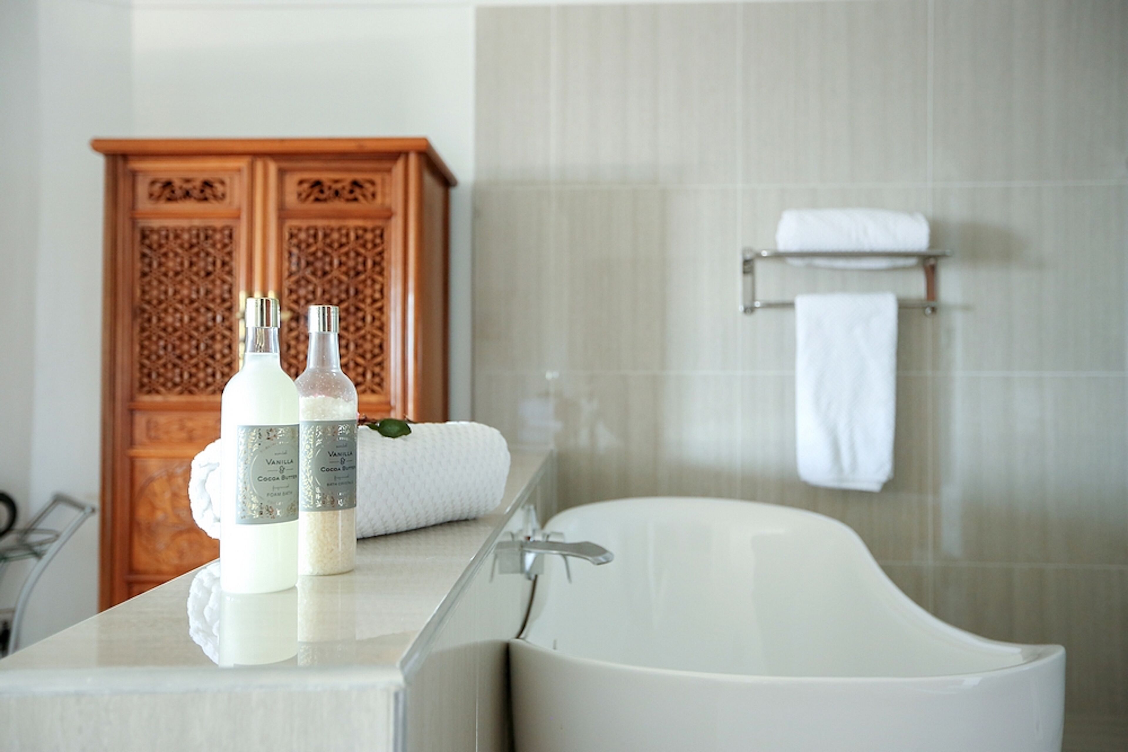 A bathroom with a bathtub, a wooden cabinet, and two bottles of bath products on a counter.
