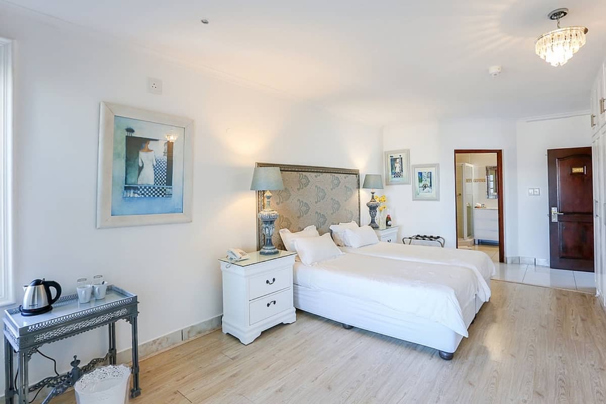 Une chambre à coucher avec un grand lit, des tables de chevet, une commode, un lustre et des œuvres d’art accrochées aux murs.