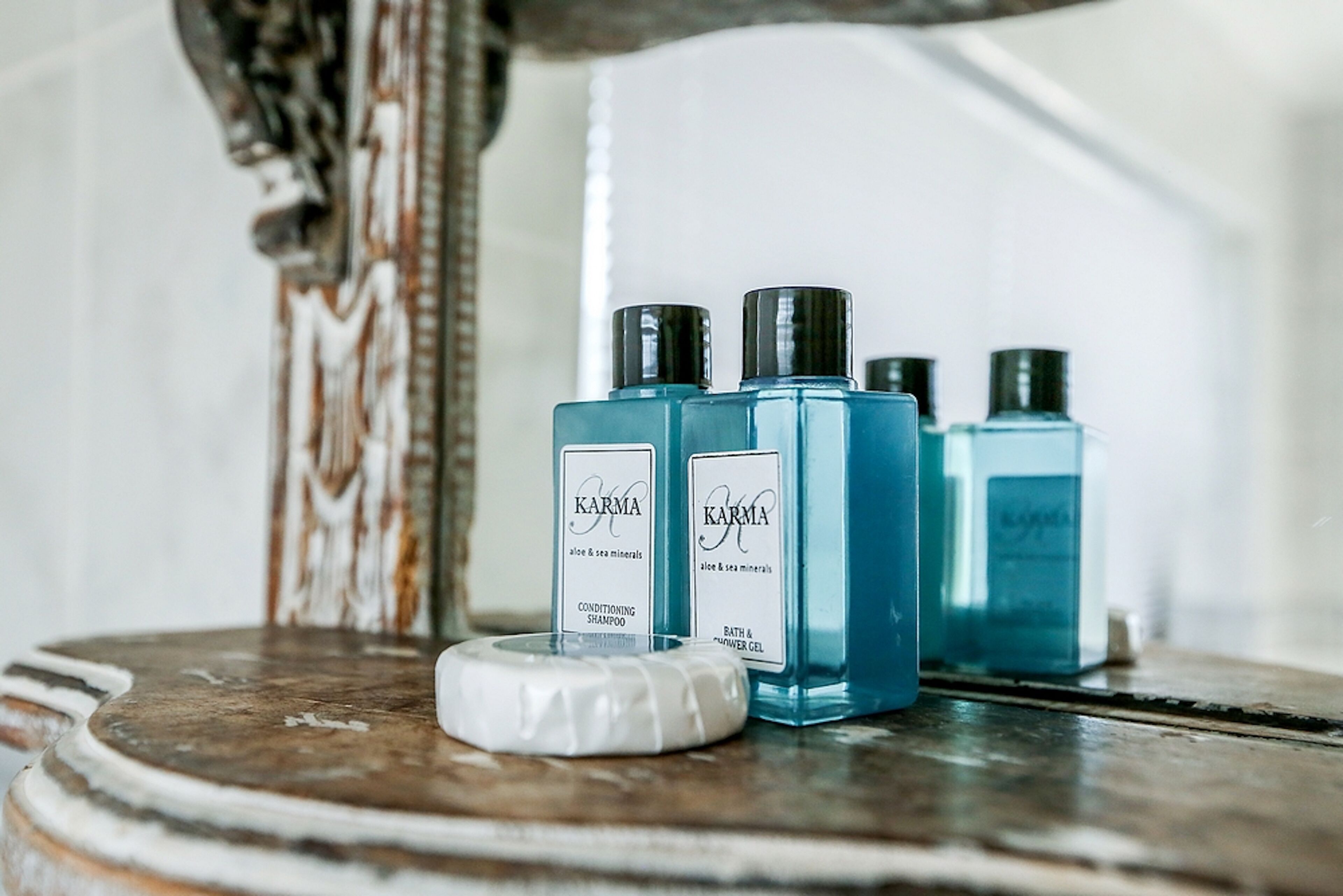 Three blue bottles of KARMA conditioning shampoo and bath & shower gel on a wooden surface.