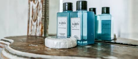 Three blue bottles of KARMA conditioning shampoo and bath & shower gel on a wooden surface.