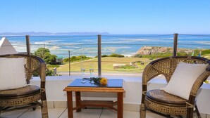 A balcony with wicker chairs and a small table, overlooking a coastal landscape. - Misty Waves Boutique Hotel (Hermanus)