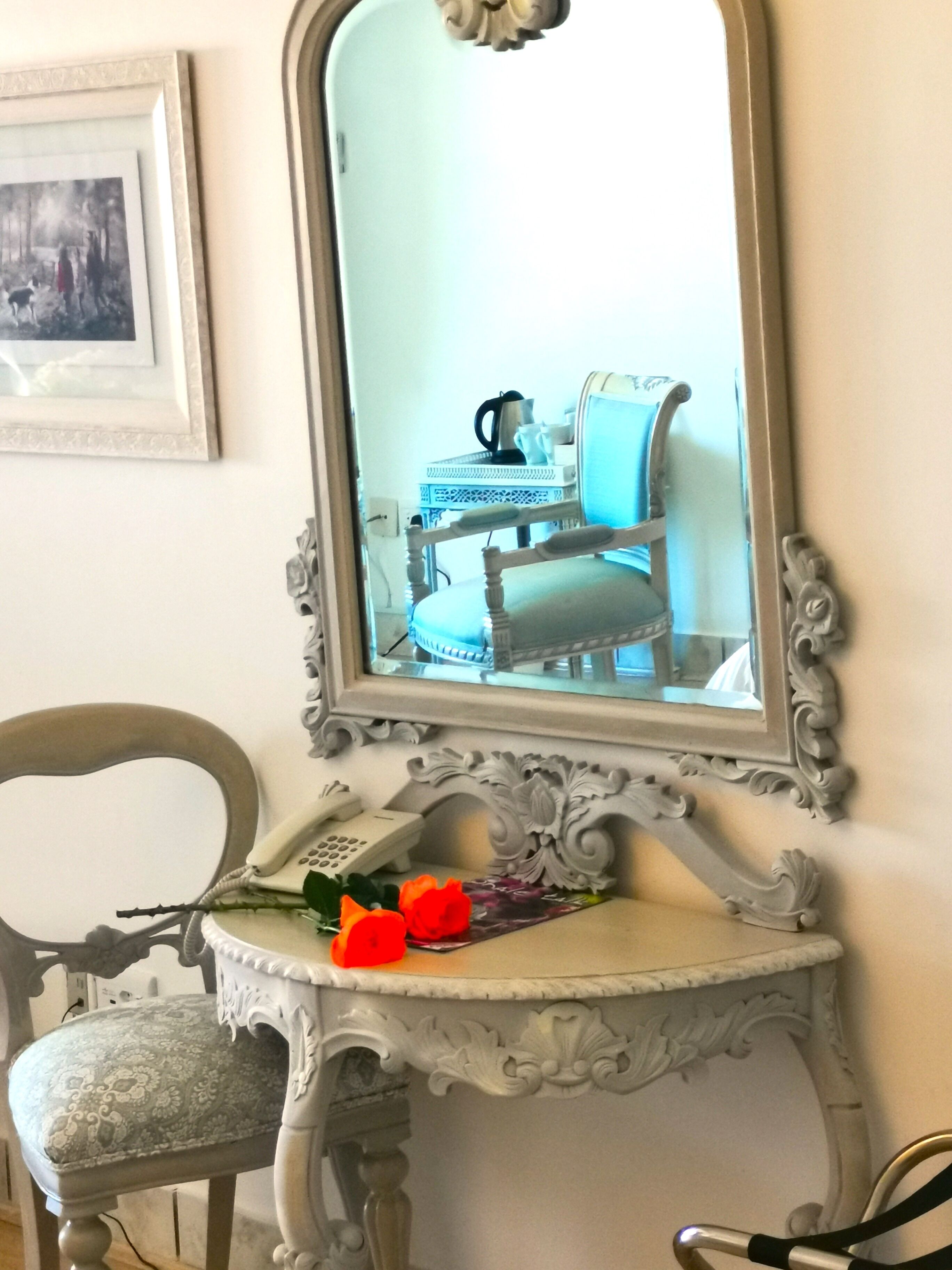 Un tocador de estilo vintage con espejo, un teléfono y un florero con flores.