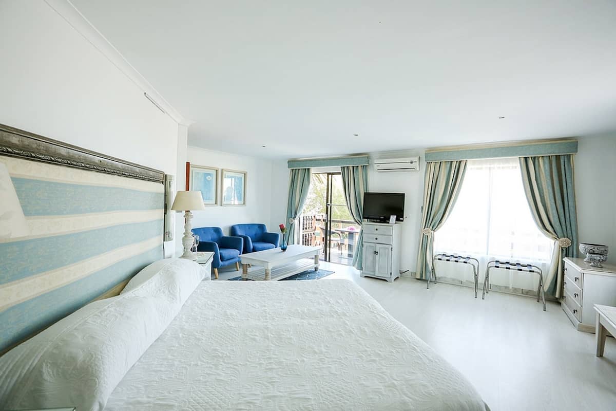 Une chambre d’hôtel avec un grand lit, un bureau doté d’un téléviseur à écran plat, deux chaises bleues et une fenêtre avec des rideaux.