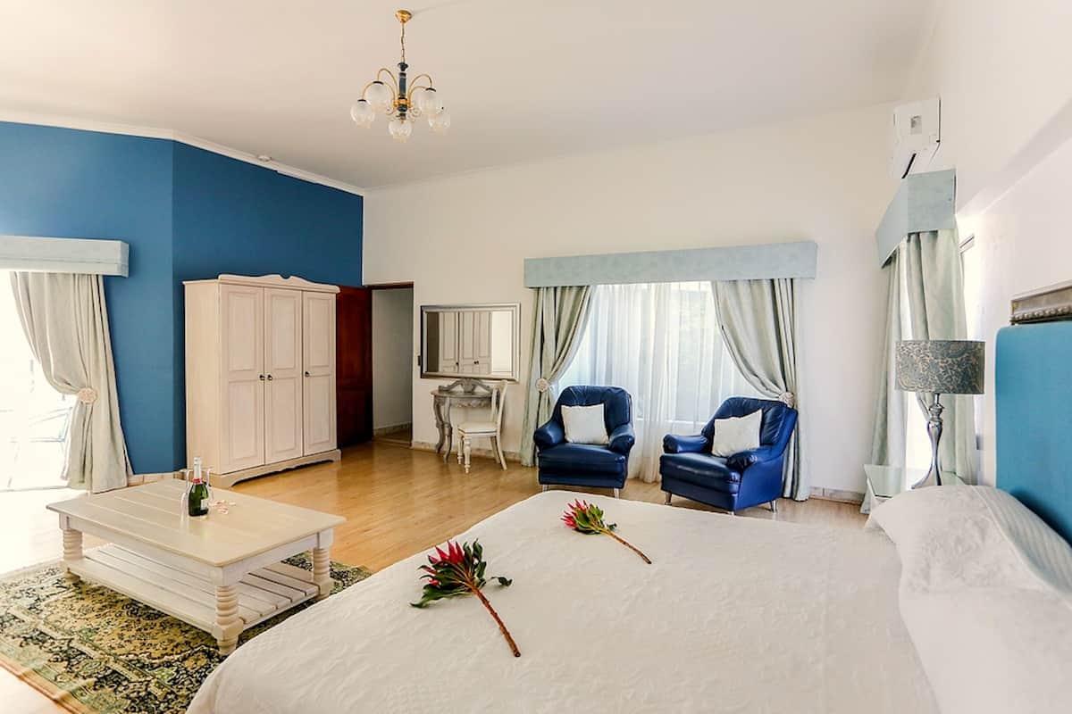 Une chambre à coucher avec un grand lit, deux fauteuils bleus, une armoire blanche et une petite table sur laquelle se trouve une bouteille.