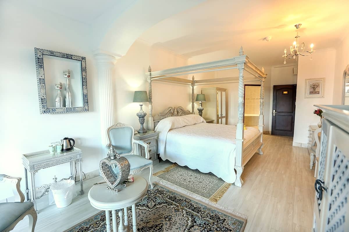 Une chambre à coucher avec un lit à baldaquin, une table de chevet avec une lampe, une chaise et une petite table ornée d’un objet décoratif.